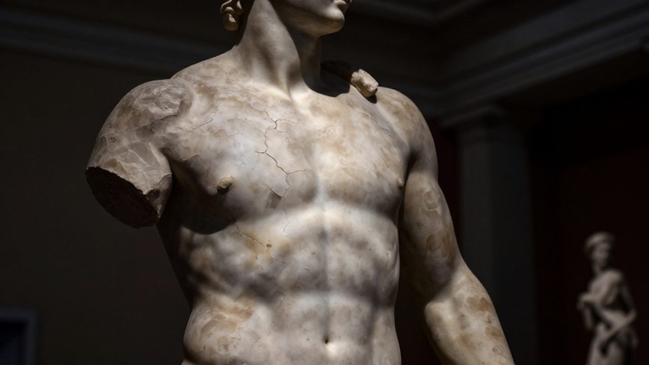 Estatua de mármol de Hércules con texturas desgastadas bajo un foco de luz en un museo.